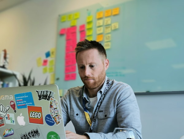 Francis Rowland sat working on his laptop with post-its stuck to the wall behind him out of focus